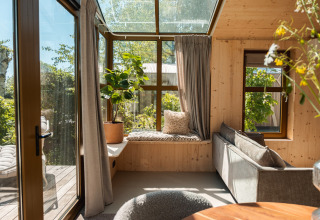 Soggiorno luminoso al Large Green House Lodge nei Paesi Bassi, con vetrate, piante e angolo relax.