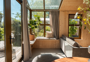 Zonnige leefruimte in Large Green House Lodge, Nederland, met glazen plafond, planten en zitbankje.