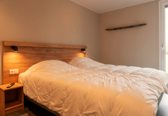 Knusse lodge slaapkamer met tweepersoonsbed, houten accenten en warme verlichting naast het raam.
