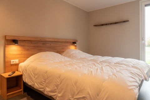 Accogliente camera da letto in un lodge con letto matrimoniale, decorazioni in legno e luce soffusa vicino alla finestra.