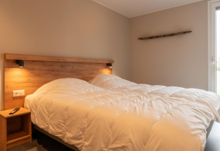 Accogliente camera da letto in un lodge con letto matrimoniale, decorazioni in legno e luce soffusa vicino alla finestra.