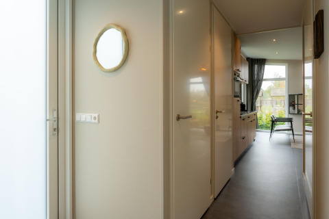 Corridoio luminoso in un lodge con porta, specchio a parete, accesso alla cucina e vista sul soggiorno.