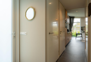 Corridoio luminoso in un lodge con porta, specchio a parete, accesso alla cucina e vista sul soggiorno.