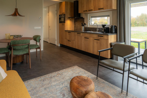Interno lodge moderno con cucina in legno, sedie verdi, grandi finestre e atmosfera accogliente.
