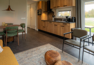 Interno lodge moderno con cucina in legno, sedie verdi, grandi finestre e atmosfera accogliente.