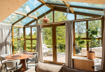 Zonnige leefruimte in ‘Large Green House 4 persons’ lodge met glazen dak en tuinzicht in Nederland.