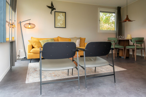 Soggiorno moderno presso il lodge Yn 't Bosk 12 nei Paesi Bassi con divano giallo e zona pranzo.