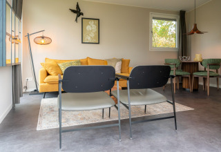 Soggiorno moderno presso il lodge Yn 't Bosk 12 nei Paesi Bassi con divano giallo e zona pranzo.