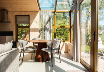 Zonnige eetruimte in de Large Green House lodge in Nederland, met glaswanden en tuinzicht.