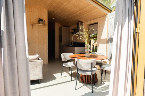 Interno di un moderno lodge in legno con tavolo rotondo, quattro sedie e cucina nel Large Green House, Paesi Bassi.