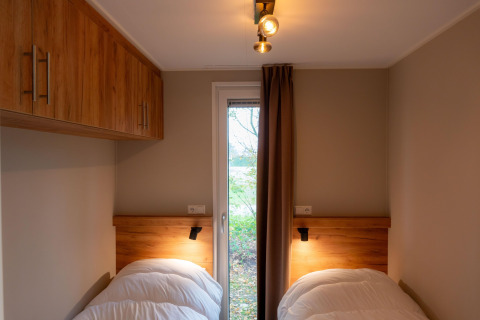 Accogliente camera da letto in lodge con letti singoli, armadi in legno e porta sul verde esterno.