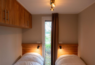 Accogliente camera da letto in lodge con letti singoli, armadi in legno e porta sul verde esterno.