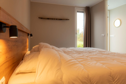 Camera accogliente in un lodge con letto matrimoniale, testiera in legno e luce naturale dalla finestra.