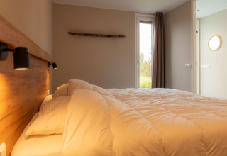 Camera accogliente in un lodge con letto matrimoniale, testiera in legno e luce naturale dalla finestra.
