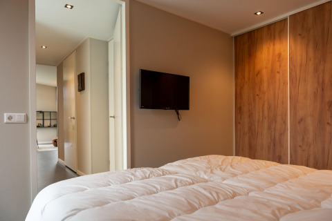 Camera da letto moderna in lodge con TV a parete, armadio in legno e vista verso il corridoio.