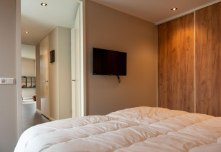 Camera da letto moderna in lodge con TV a parete, armadio in legno e vista verso il corridoio.