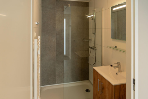 Bagno moderno in lodge con doccia in vetro, mobile in legno, lavabo e specchio illuminato.