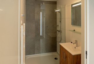 Bagno moderno in lodge con doccia in vetro, mobile in legno, lavabo e specchio illuminato.