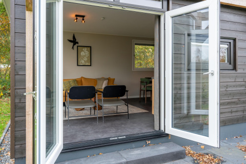 Porte patio aperte verso un'accogliente lodge con divano, sedie e arte alle pareti, vista dall'esterno.