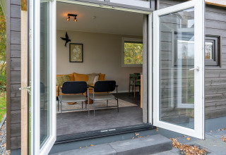 Porte patio aperte verso un'accogliente lodge con divano, sedie e arte alle pareti, vista dall'esterno.