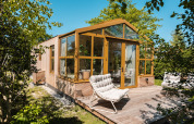 Beeld van lodge ‘Large Green House 4 persons’ in Nederland met glazen voorzijde, houten terras en loungestoelen.