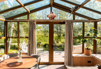 Sollys strømmer ind i en moderne lodge med glastag, naturlige trærammer og udsigt over naturen.