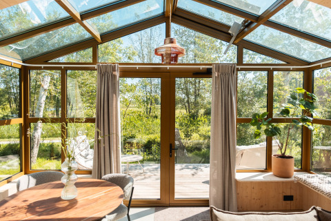 Luce naturale filtra in un lodge moderno con tetto in vetro, cornici in legno e vista sul verde esterno.