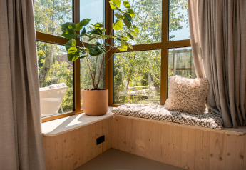 Solrig karnap i "Large Green House" lodge med bløde puder, potteplante og udsigt til grøn natur.