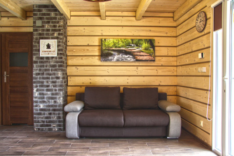 Salón con sofá marrón, paredes de madera y arte mural en Holiday home «Maryna», chalet en Alemania.