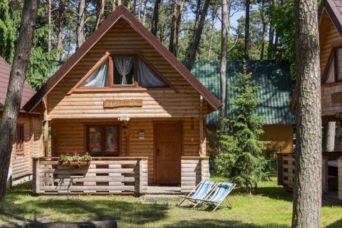 Houten chalet in Pobierowo te midden van het bos, met terras, bloemenbak en ligstoelen in het gras.