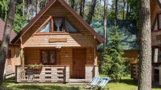 Wooden holiday cottage in Pobierowo, surrounded by trees, with a porch, flowers, and sun loungers outside.
