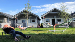 Twee mensen ontspannen op stoelen en een hangmat voor Aquarius Cottages op een zonnig gazon.