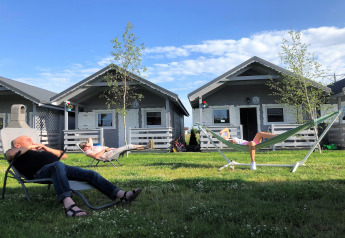 Relaxing outside Aquarius Cottages, two people lounge on chairs and hammock in sunny grassy yard.