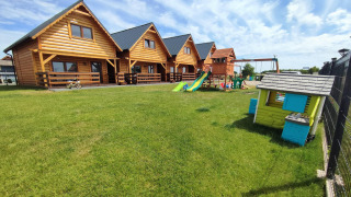 Cabañas de madera en Lazurowy Zakątek con zona infantil y césped verde bajo un cielo azul claro.