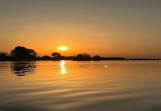 Tramonto sereno sull'acqua, visto dal lodge «Yn 't Bosk 14» nei Paesi Bassi, alberi in controluce.