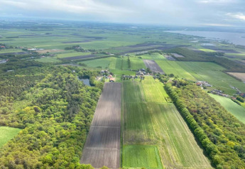 Vista aérea de un lodge rodeado de campos verdes, bosques y tierras de cultivo bajo un cielo nublado.