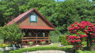 Incantevole casa su una collina con portico in legno, circondata da fiori rossi e verde rigoglioso.