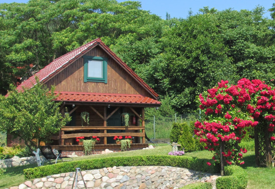 Charmant huis op een heuvel met houten veranda, omgeven door rode bloemen en groen gebladerte.