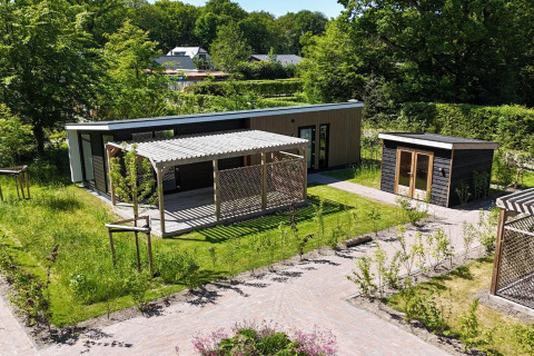 Lodge moderno 'Op'e Pleats 1' nei Paesi Bassi con pergolato, giardino e ambiente verde circostante.