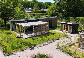 Lodge moderno 'Op'e Pleats 1' nei Paesi Bassi con pergolato, giardino e ambiente verde circostante.