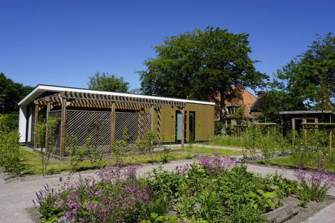 Lodge moderno presso Op'e Pleats 1 nei Paesi Bassi con giardino, piante verdi e cielo sereno.