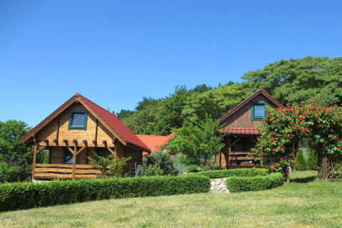 Twee sfeervolle houten lodges met rode daken, omgeven door groen, struiken en bloemen in de tuin.
