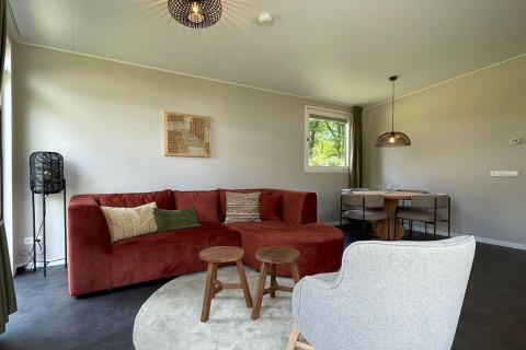 Soggiorno moderno al lodge «Op'e Pleats 1» nei Paesi Bassi, con divano rosso e zona pranzo.