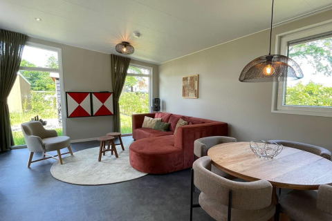 Soggiorno moderno all'interno del lodge Op'e Pleats 1 nei Paesi Bassi, con divano rosso e tavolo rotondo.