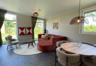 Soggiorno moderno all'interno del lodge Op'e Pleats 1 nei Paesi Bassi, con divano rosso e tavolo rotondo.