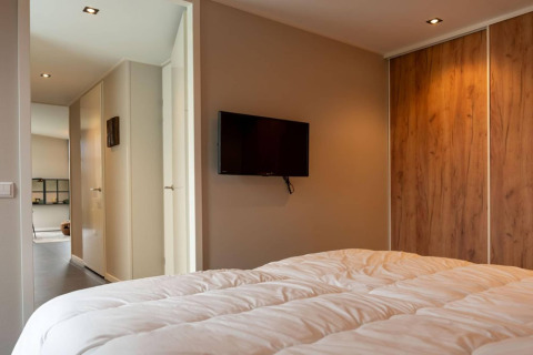 Camera da letto con piumone bianco, TV a parete e armadio in legno del lodge Op'e Pleats 1 nei Paesi Bassi.