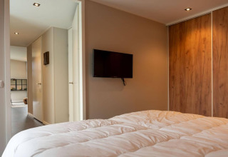 Camera da letto con piumone bianco, TV a parete e armadio in legno del lodge Op'e Pleats 1 nei Paesi Bassi.