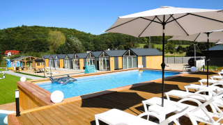 Piscina al aire libre con tumbonas y sombrillas frente a cabañas en Turkusowa osada Wapnica.