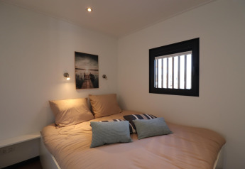 Chambre avec lit double, coussins, fenêtre à barreaux et tableau sur Houseboat « Refugio » aux Pays-Bas.