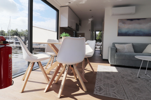 Moderne stue og spiseplads på husbåd Refugio i Holland med store vinduer og udsigt til vandet.